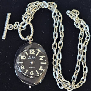 Necklace, silver tone chain with black 1 1/8 x 1 1/2 " Oval pendant with round watch face, 18" chain, toggle closure